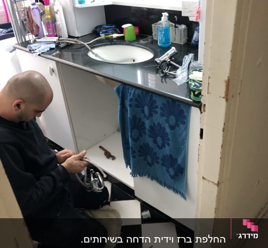 אינסטלטור עובד מתחת לכיור עם כלים וצינורות